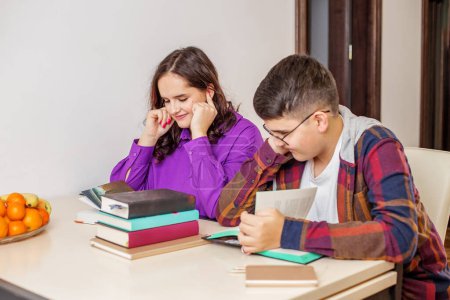 Zwei glückliche Teenager, Junge und Mädchen, lernen zusammen mit Büchern auf dem Tisch und genießen das gemeinsame Lernen zu Hause.