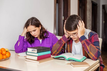 Teenage girl and boy look stressed while studying pile of books, indicating pressure of preparing for school exams at home
