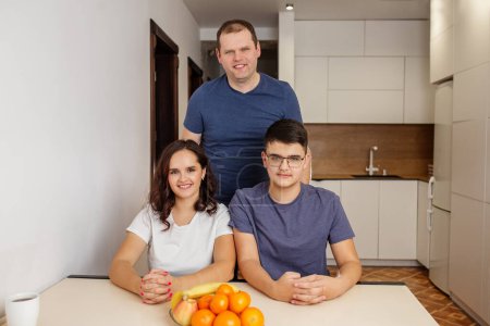 Happy family of three sitting in well-lit modern kitchen with fresh fruits on table