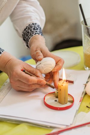 Hände, die vor dem Färben Wachs auf das weiße Ei auftragen, klassische Methode im Ostereierschmuck.