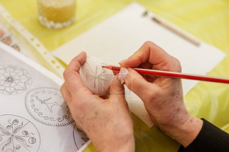 Großaufnahme von Händen, die weißes Osterei mit Bleistift markieren, umgeben von Färbewerkzeugen.