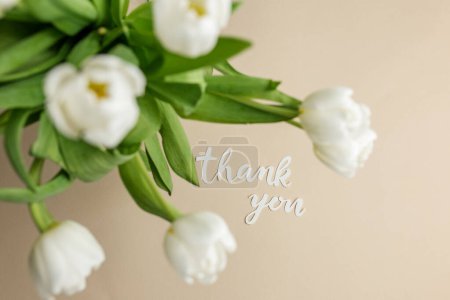 Soft beige background with white tulips and cursive 'thank you' message, conveying warm appreciation.