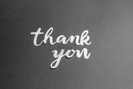 Sincere 'thank you' message, stylishly presented in white paper cutout letters on textured dark grey surface.