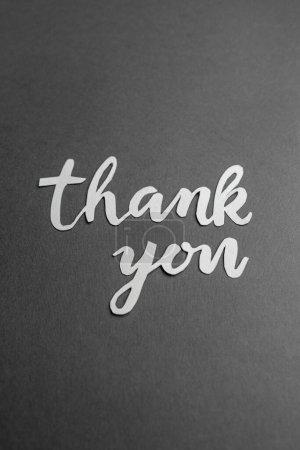 Sincere 'thank you' message, stylishly presented in white paper cutout letters on textured dark grey surface.