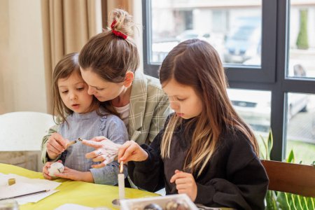 Un tierno momento familiar como madre enseña a sus dos hijas el arte de la decoración de huevos de Pascua en su casa.