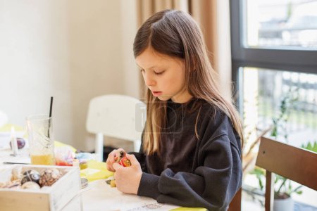 Young girl with brown hair is deeply concentrated on painting a colorful Easter egg, embodying the spirit of holiday.
