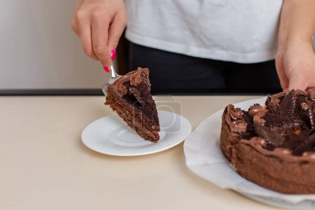 Person serves delicious slice of multi-layer chocolate cake onto a white plate, showcasing intricate chocolate frosting details.