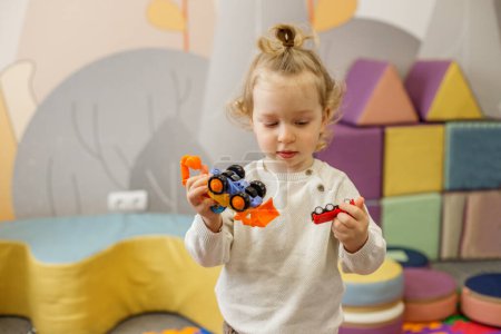 Focused toddler girl plays with colorful toy cars in vibrant, playful nursery environment.