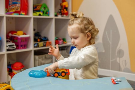Little boy examines her toy truck with focus and curiosity while playing alone in home playroom.