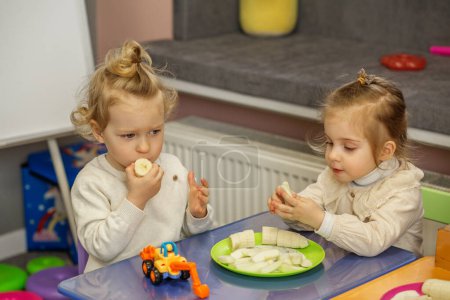 Deux tout-petits partagent une collation sur une table de jeu colorée, s'engageant ensemble dans une activité sociale et d'apprentissage.
