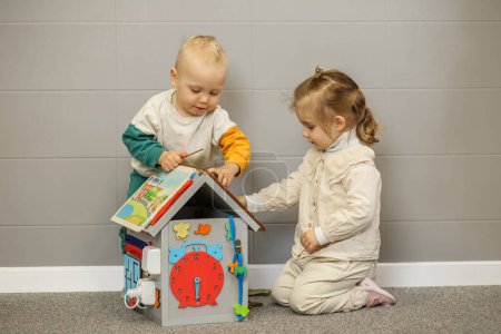 Zwei fokussierte Kleinkinder beschäftigen sich mit einer pädagogischen Aktivitätsbox, erkunden und lernen gemeinsam auf Teppichboden.