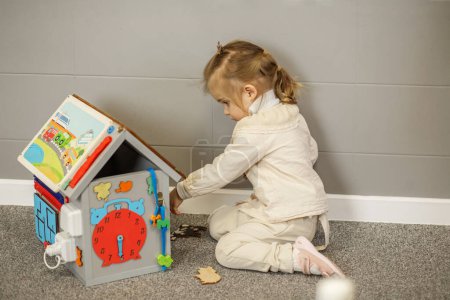 Kleines Mädchen spielt mit buntem Lernspielzeughaus und verbessert damit ihre kognitiven Fähigkeiten.