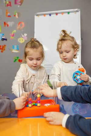 Zwei Kleinkinder sind während einer pädagogischen Spielstunde im Klassenzimmer mit dem Sortieren bunter Perlen beschäftigt.