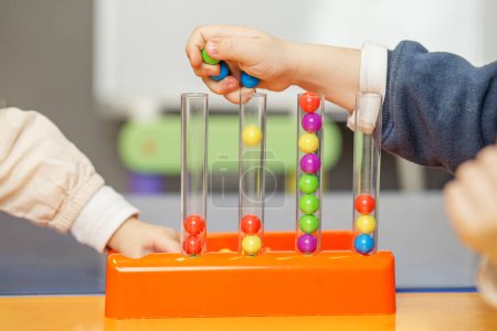Nahaufnahme der Kinderhand, die bunte Kugeln in passende Abschnitte eines Lernspielzeugs platziert, das die kognitiven Fähigkeiten verbessern soll.