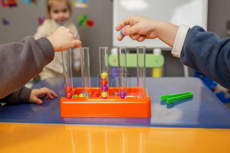 Las manos de los niños se ven jugando con un juego de clasificación de bolas y tubos, mejorando las habilidades motoras finas y el reconocimiento de color.