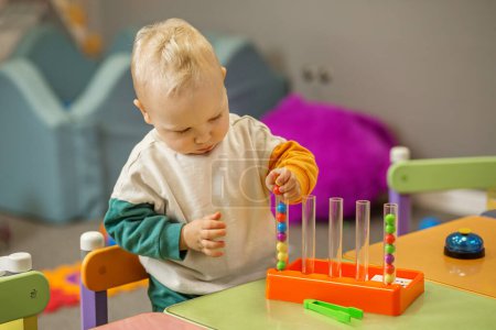 Curious toddler enjoying bead sorting toy, learning colors and coordination in vibrant playroom environment.