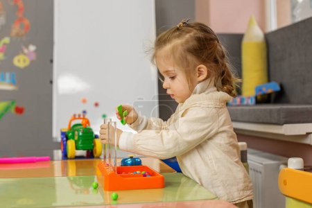 Preschool girl deeply focused on bead sorting task, developing cognitive and motor skills in an educational setting.