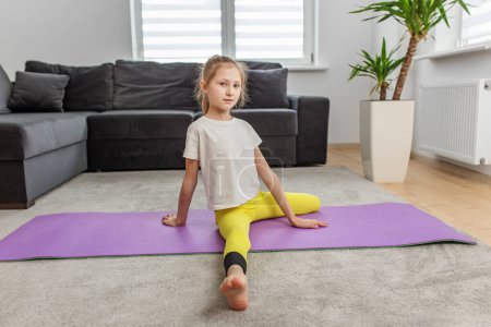 Téléchargez les photos : Preteen enfant en flexion vers l'avant étirer sur tapis de yoga violet, en se concentrant sur la flexibilité dans l'environnement de la maison. - en image libre de droit