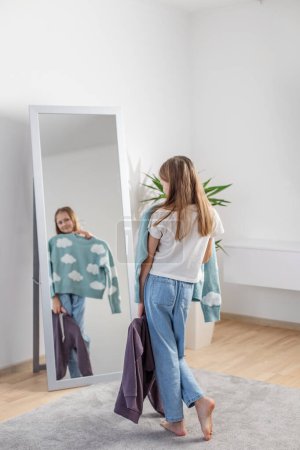 Mädchen untersucht ihre Outfit-Optionen, die sich in einem Ganzkörperspiegel widerspiegeln, umgeben von einem gemütlichen Ambiente mit Zimmerpflanze.