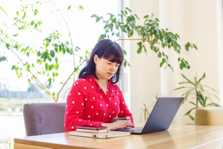 Konzentrierte Frau in leuchtend roter Bluse arbeitet intensiv am Laptop in einem Raum voller natürlichem Licht und Grün.