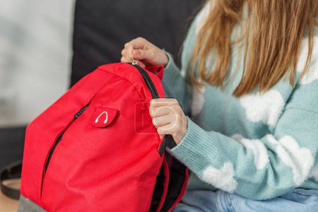 Detail shot of children's hand zipping up a vibrant red backpack, focus on everyday preparation.