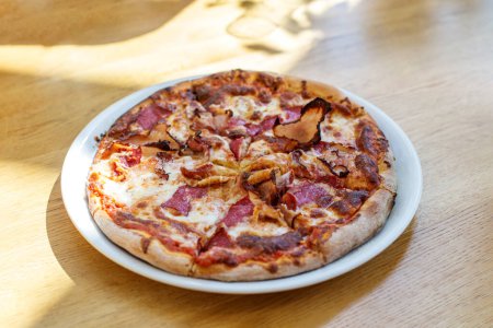 Delicious freshly baked meat lover's pizza with crispy bacon, pepperoni, and melted cheese on white plate.