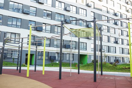 Modern outdoor playground equipment set in residential area with colorful structures and apartment buildings in background.