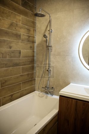 Modernes Badezimmer präsentiert elegante Badewanne mit stilvollen Holzpaneelen und einem fortschrittlichen Duschsystem, ergänzt durch einen runden beleuchteten Spiegel.