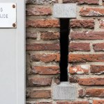 Old-fashioned Belgian bluestone letterbox without flap in historic old brick wall with a little sign on door post saying entrance other side, Utrecht city center, The Netherlands. High quality photo
