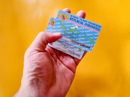 Mann mit zwei indonesischen Staatsbürgerausweisen auf gelbem Hintergrund. Foto-Illustration von Indonesiens Personalausweis. KTP. perfekt für Artikel oder andere identitätsbezogene Fragen.