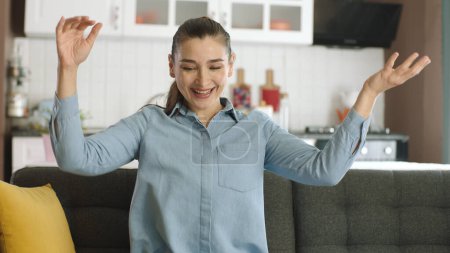 Photo for Happy young woman celebrating success with applause. Excited young woman in her seat at home clapping, having fun, rejoicing. Concept of happiness, party, winning. - Royalty Free Image