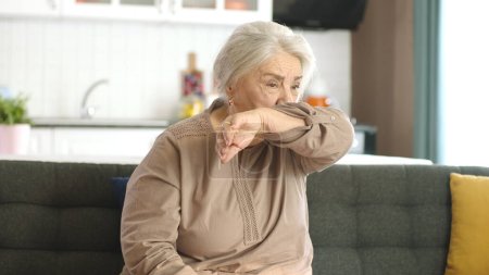 Téléchargez les photos : Les premiers symptômes du rhume et du virus de la grippe sont apparus chez la vieille femme. Femme souffrant de manque d'oxygène et d'essoufflement alors qu'elle était assise à la maison. Allergie, éternuements. - en image libre de droit