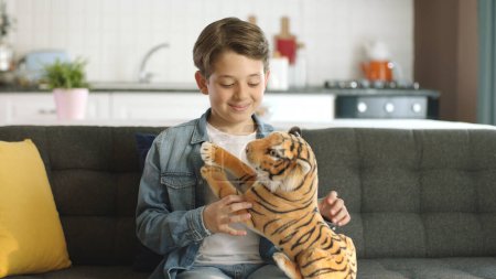 Hogar solo, niño pequeño sin amigos juega con un tigre de juguete.Tigre de juguete marrón en la mano del niño. Niño jugando con un tigre de juguete en el salón.