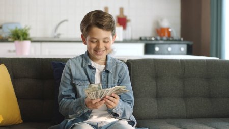 Photo for Beautiful little boy very happy with his money.Winning the online lottery lottery. The boy is making a fan out of dollars. Excited little boy enjoying his dollar at home alone. - Royalty Free Image