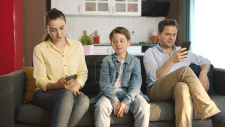 Demanding attention from his young parents, the little boy is bored with the plight of his tech-addicted parents.Technology addicted couple looking at their social media accounts on their smartphones.