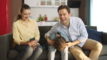 Porträt von Eltern, die sich um ihre Kinder kümmern. Junges Paar verbringt Zeit mit ihrem kleinen Sohn im Wohnzimmer ihres Hauses. Glücklich lächelndes Familienporträt.