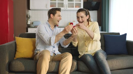 Photo for A young man gives his girlfriend a beautiful ring as a Valentine's Day gift. Young man showing engagement ring to his girlfriend at home. Marriage proposal. - Royalty Free Image