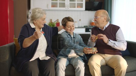 Téléchargez les photos : Petit garçon rendant visite à ses grands-parents. Petit garçon mangeant des bonbons colorés avec ses grands-parents. Portrait d'un visiteur pendant l'Aïd al-Adha ou l'Aïd al-Ramadan. - en image libre de droit