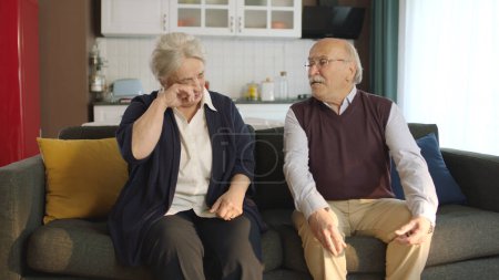 Téléchargez les photos : Un couple âgé assis dans son fauteuil à la maison. Image d'un couple âgé dans des mariages troublés. Vieil homme réconfortant sa femme triste qui pleure. - en image libre de droit