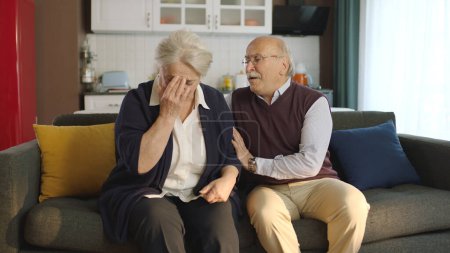 Photo for An elderly couple sitting in their armchair at home. Image of an elderly couple in troubled marriages. Old man comforting his crying, sad wife. - Royalty Free Image