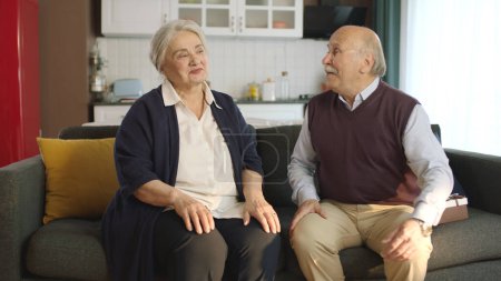 Glückliche ältere Paare sitzen in ihren Sesseln in ihrem friedlichen Zuhause und unterhalten sich. Bild eines lange verheirateten älteren Ehepaares, das eine glückliche Zeit zusammen hat.