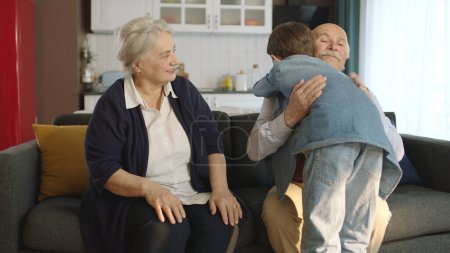 El niño visitó a su abuelo y celebró Eid al-Fitr besándose las manos. Feliz pareja de ancianos sentados en el sofá besando y abrazando a su nieto. 