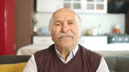 Téléchargez les photos : Portrait d'un vieil homme âgé assis sur un canapé à la maison. Vieil homme heureux posant pour la caméra, souriant. - en image libre de droit