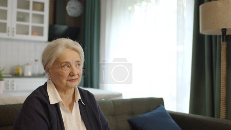 Sad, thoughtful and unhappy old woman alone at home. The worried old woman was lost in thought. Woman at home alone feeling anxious looking at empty advertising space to the right of the camera.