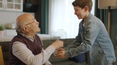 Junge bietet seinem alten Großvater Bonbons in Schale an. Kleiner Junge, der seinem älteren Großvater Süßigkeiten anbietet, um das traditionelle Eid al-Fitr (Süßigkeitenfest) nach dem Ende des Ramadan zu feiern.