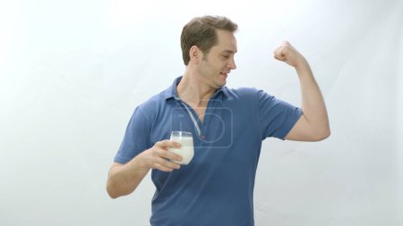 Young man with glass of milk on white background. The man drinks milk and shows his biceps. Be healthy. The power of calcium. Young man showing biceps after drinking milk on white background.