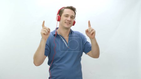 Téléchargez les photos : Man listening to mp3 radio music in wired headphones, listening to music and dancing in front of white background. Leisure activity. Man wearing wired headphones having fun while listening to music. - en image libre de droit