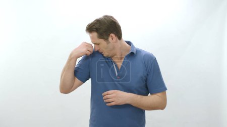 Foto de Man who is sweating heavily isolated on white background smells bad. Young man worried and showing sweating spot problem with sweating, sniffing armpit.Bad odor, excessive sweating concept. - Imagen libre de derechos