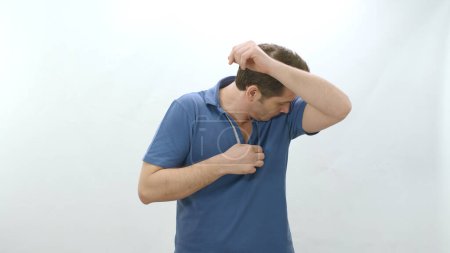 Foto de Man who is sweating heavily isolated on white background smells bad. Young man worried and showing sweating spot problem with sweating, sniffing armpit.Bad odor, excessive sweating concept. - Imagen libre de derechos