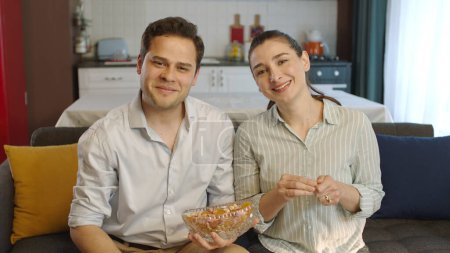 Photo for Young married couple loving each other eating mixed nuts. The woman and her husband, who eat hazelnuts, peanuts, almonds, watch movies on TV and have fun, laugh and are surprised at what they see. - Royalty Free Image